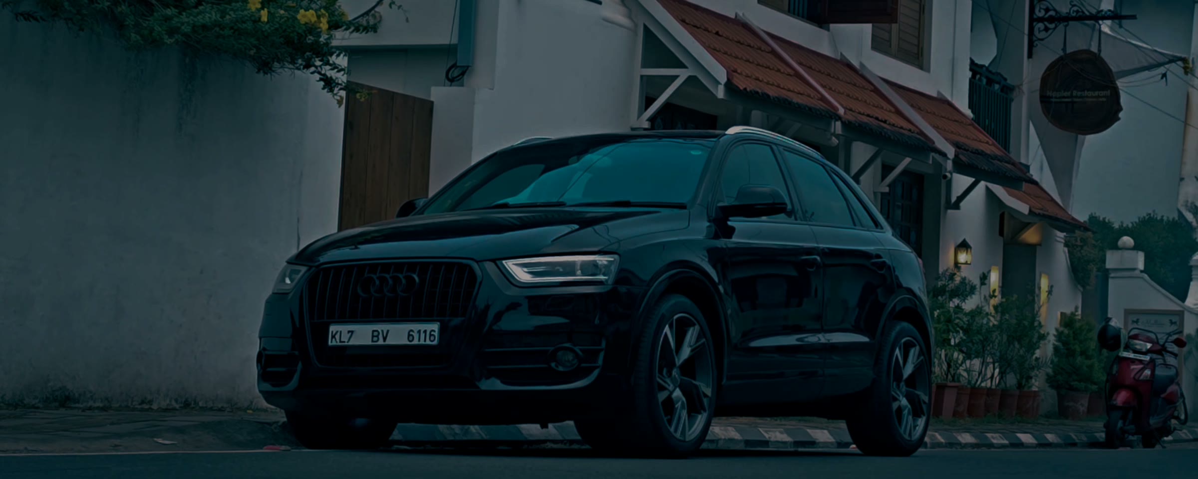 A black Audi Q3 Sportback parked outside a white house in Kochi at dusk.