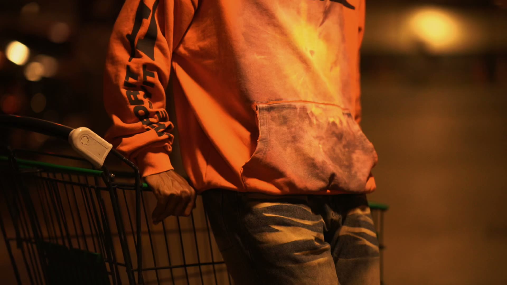 A person in an orange Qclaw sweatshirt in a warmly lit parking garage at night.